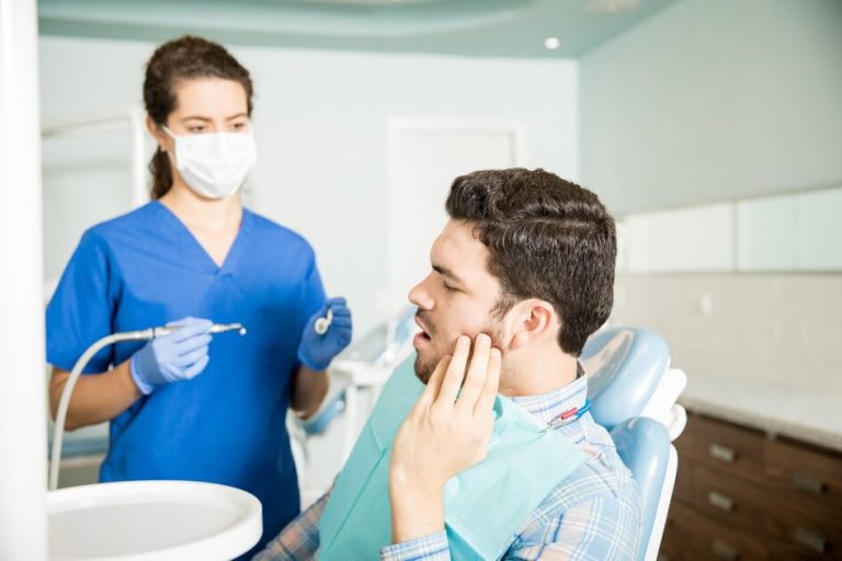 mid-adult-man-suffering-from-toothache-while-looking-dentist-with-tools-clinic (1) Root Canal vs Tooth Extraction - علاج جذور الأسنان أم خلع الأسنان